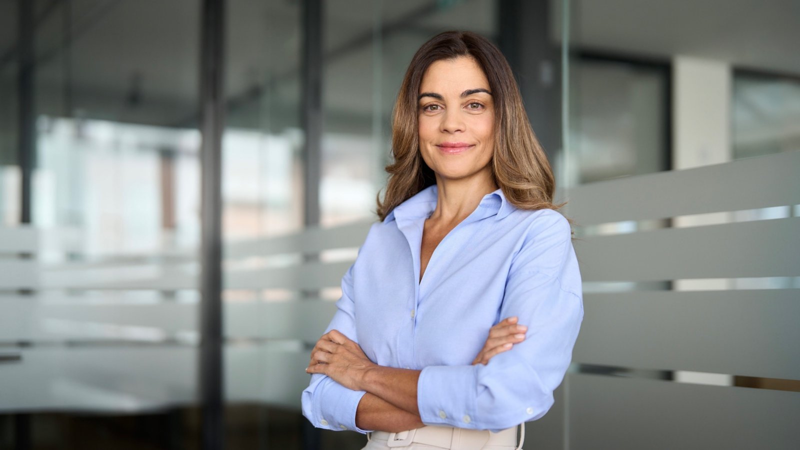 Bewirbdich.ch bringt dein Bewerbungsdossier auf den neusten Stand. Selbstbewusste Frau mit verschränkten Armen im Büro – Unterlagen-Check